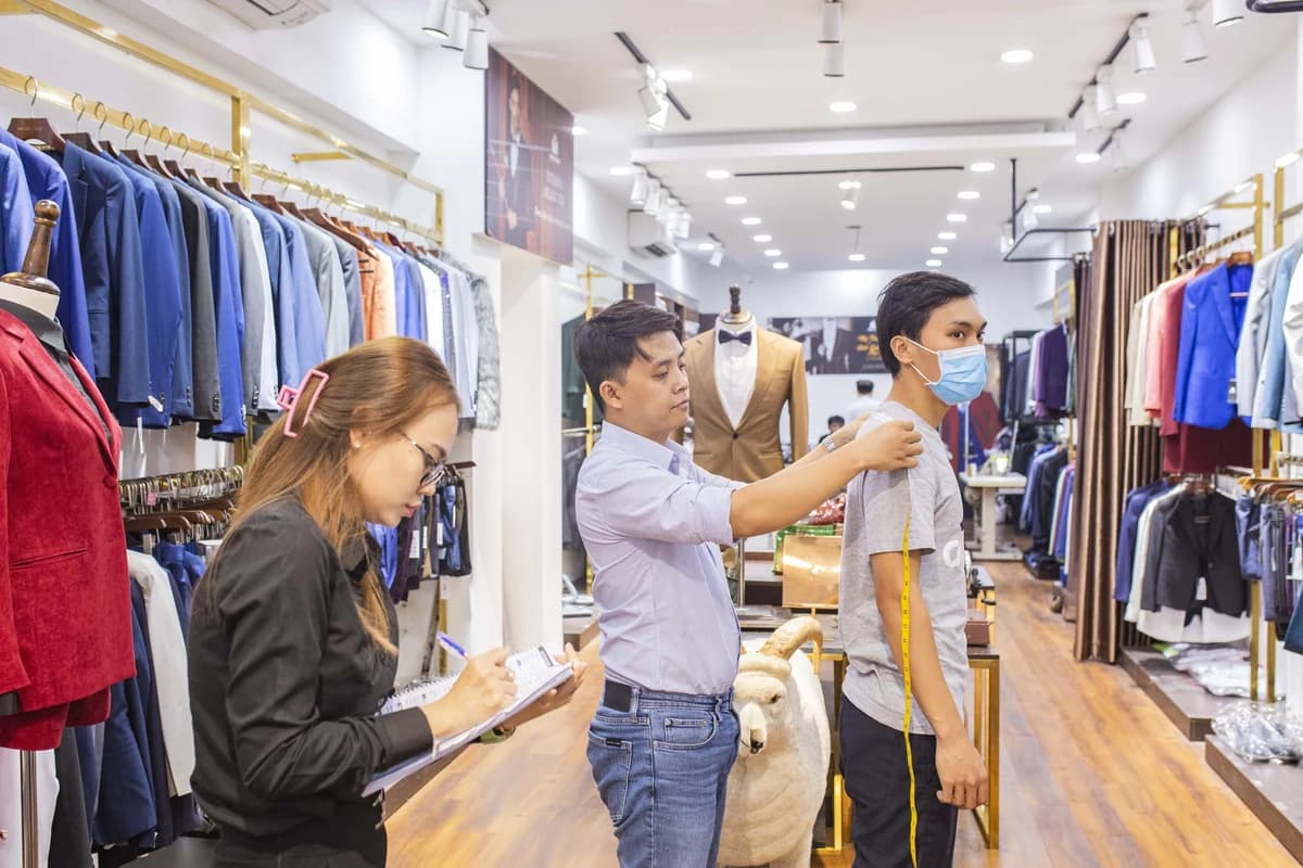 Nhân viên đo số đo cho khách trong showroom, một nhân viên ghi chép