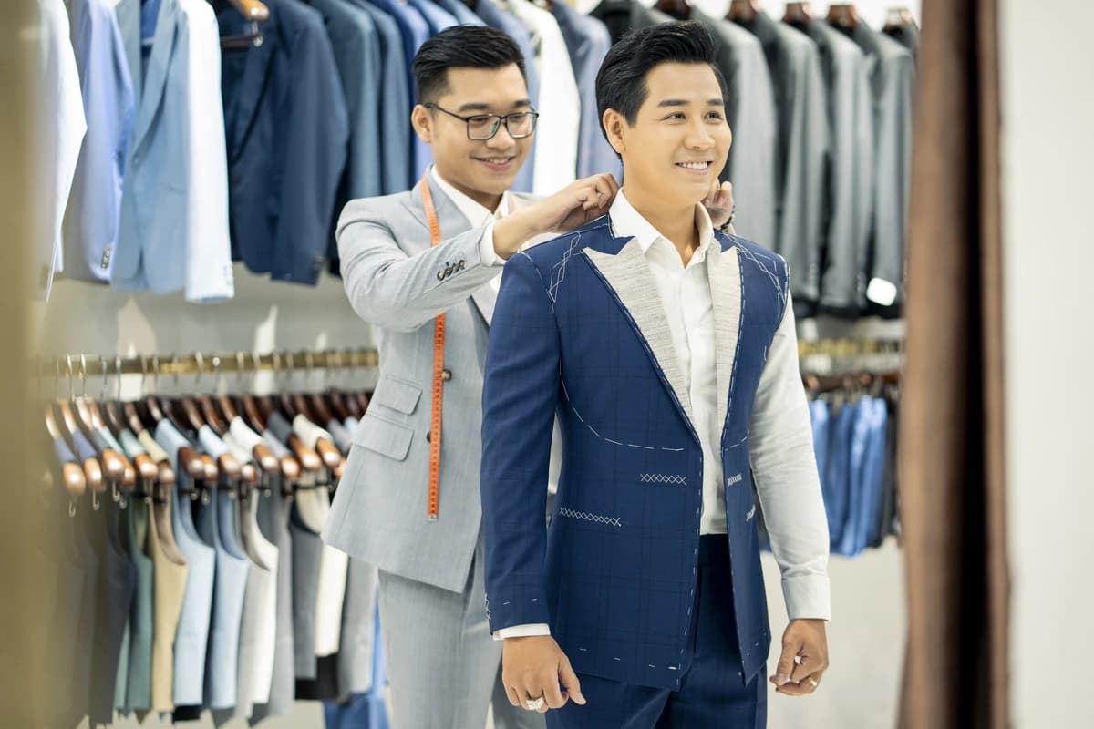 Thợ may chỉnh áo vest xanh chưa hoàn thiện cho khách thử
