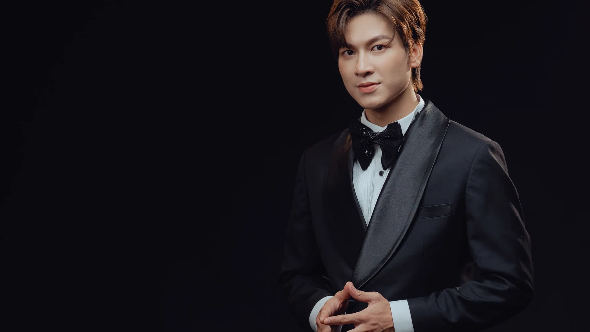 Nghệ sĩ mặc tuxedo cổ shawl, nơ đen, nền studio tối