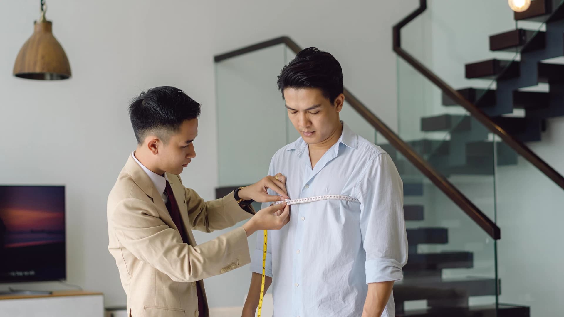 Thợ may dùng thước dây đo vai cho khách bên cầu thang kính