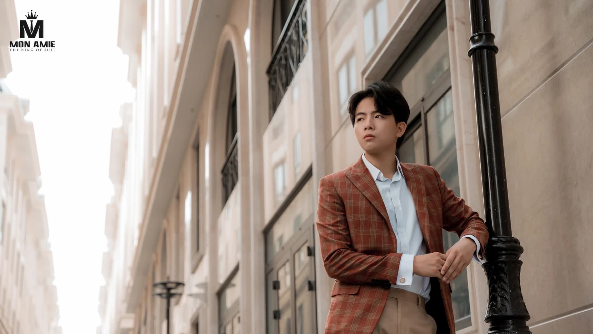 Người mẫu mặc blazer caro cam gạch dựa cột đèn trong con ngõ kiểu châu Âu