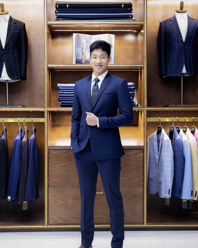 Client in a navy suit standing before fabric shelves and hanging suits